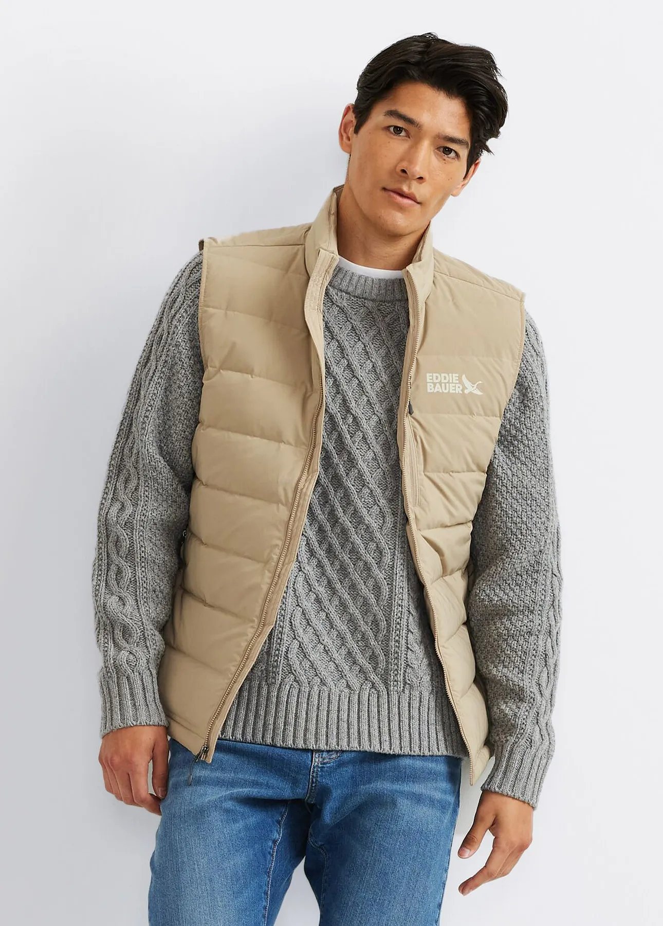 A man wearing a down vest over a cable knit sweater.