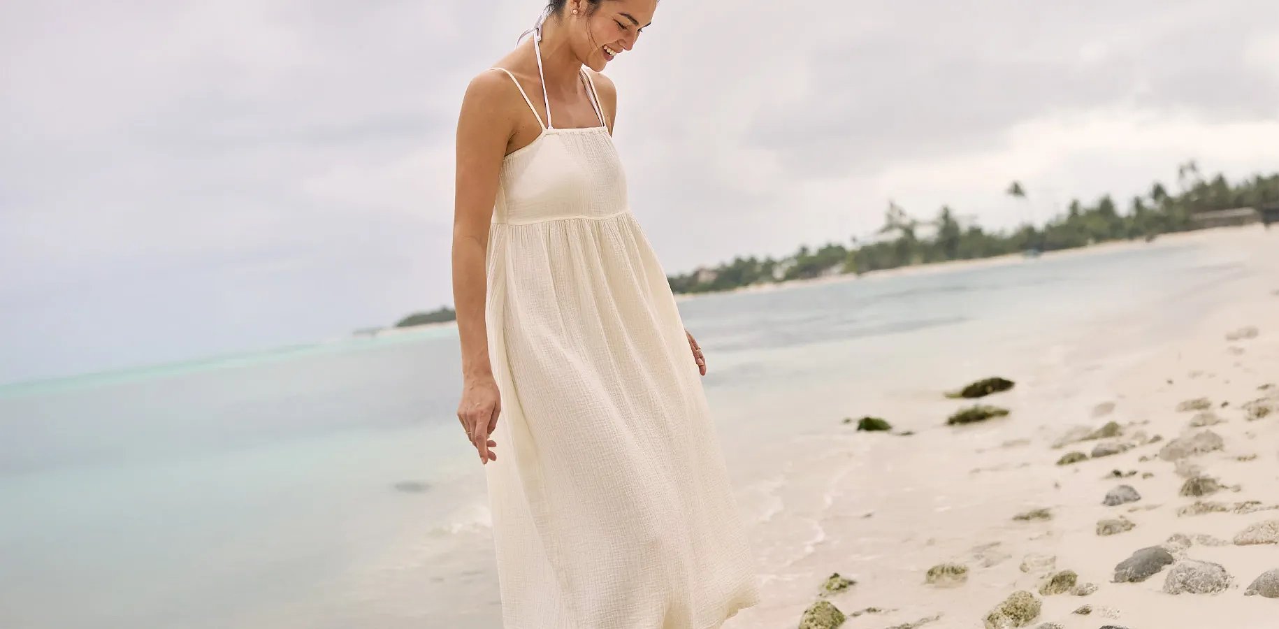 A women wearing a long flowing dress walks on the beach.