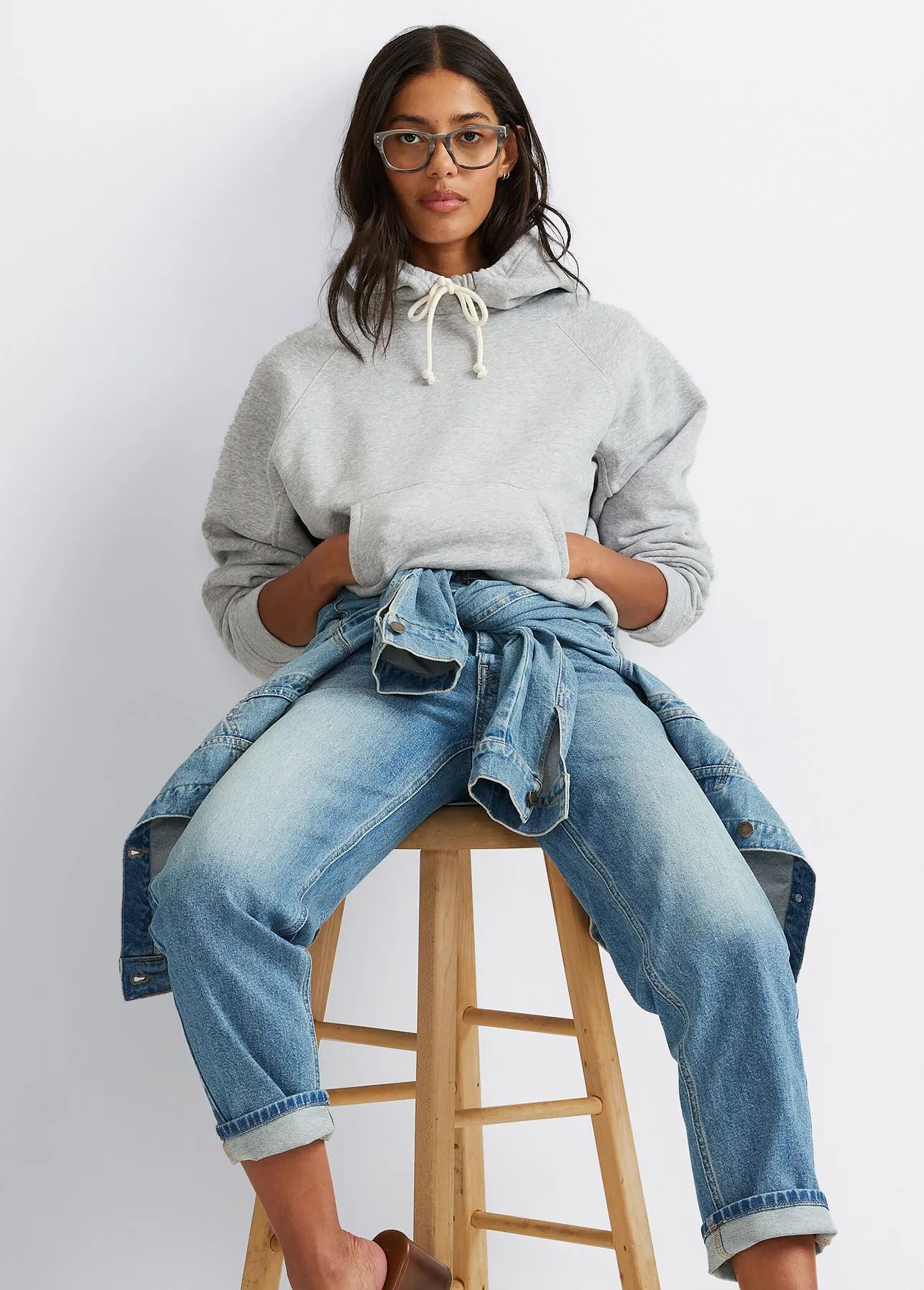 A woman wearing jeans and a sweatshirt with a denim jacket tied around her waist.