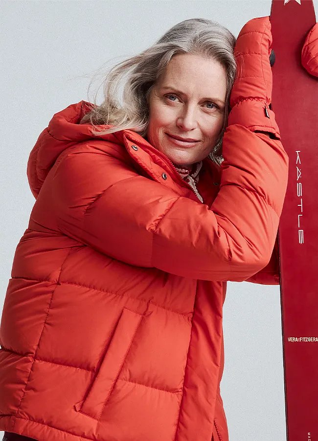 A woman wearing a down jacket leans on a pair of skis.