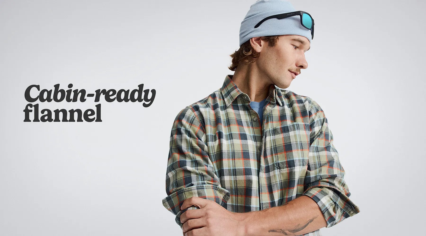 Cabin-ready flannel. A man wearing a beanie with sunglasses pushed up on his forehead & a flannel shirt.