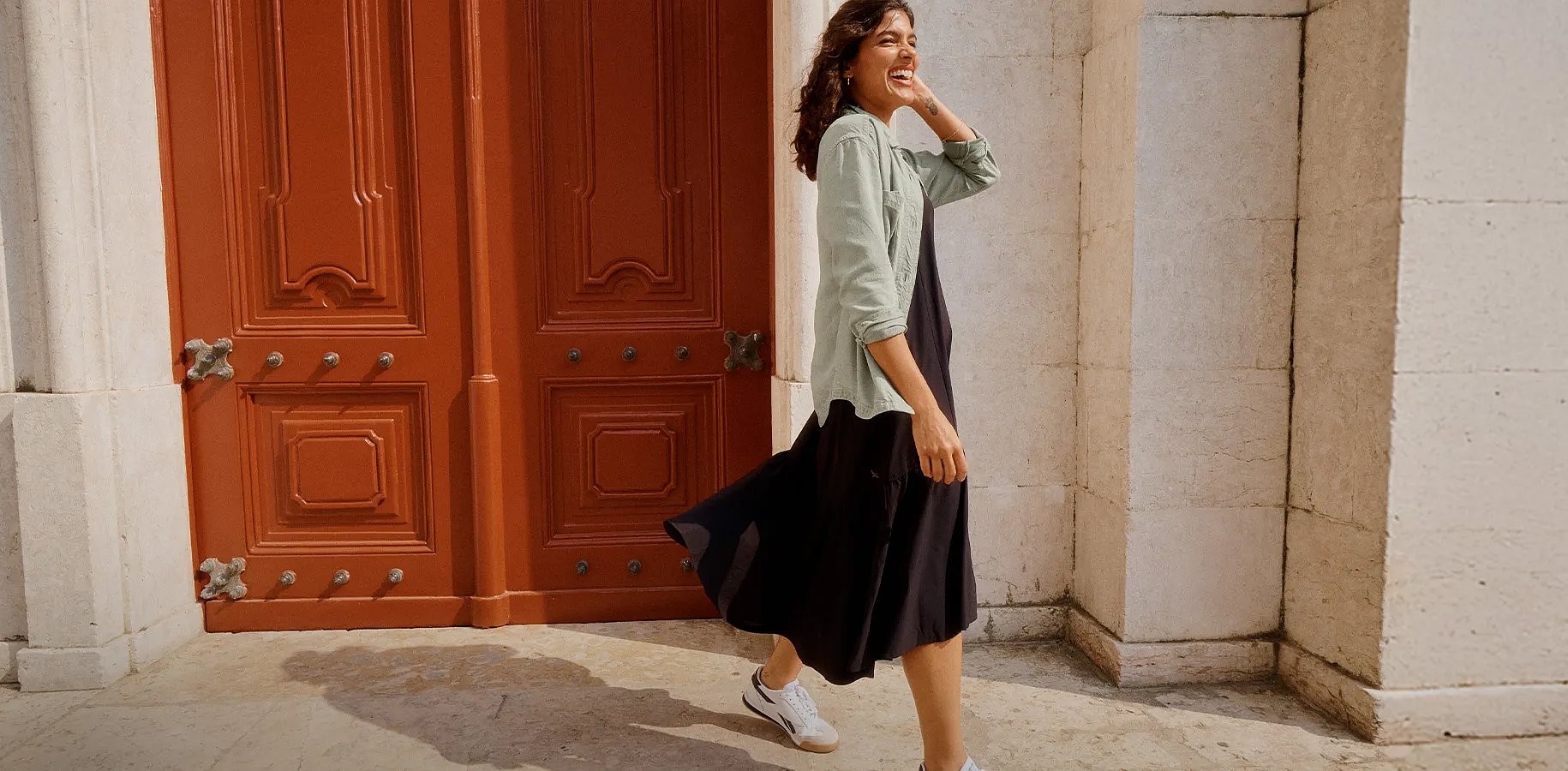 One & Done Favorites. A woman in a short shirt dress and waist pack walks along a picturesque cobblestone street.