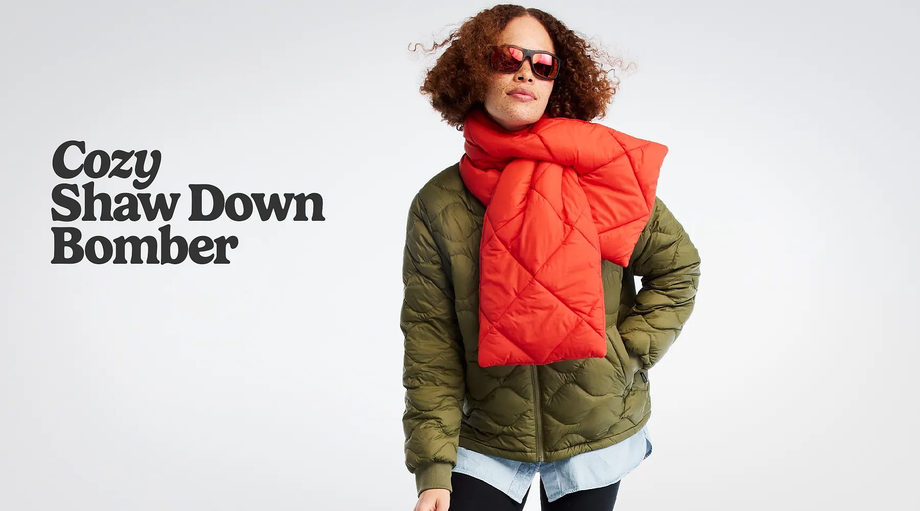 Cozy Shaw Down Bomber. A smiling women wearing sunglasses, scarf, and a down jacket.