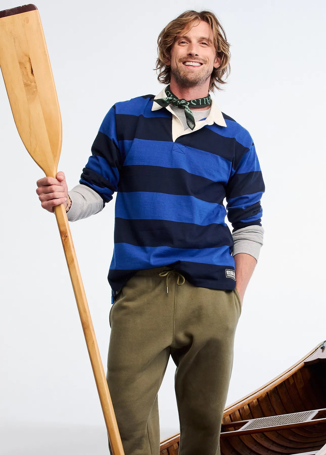A man wearing a rugby shirt stands in a canoe holding a paddle
