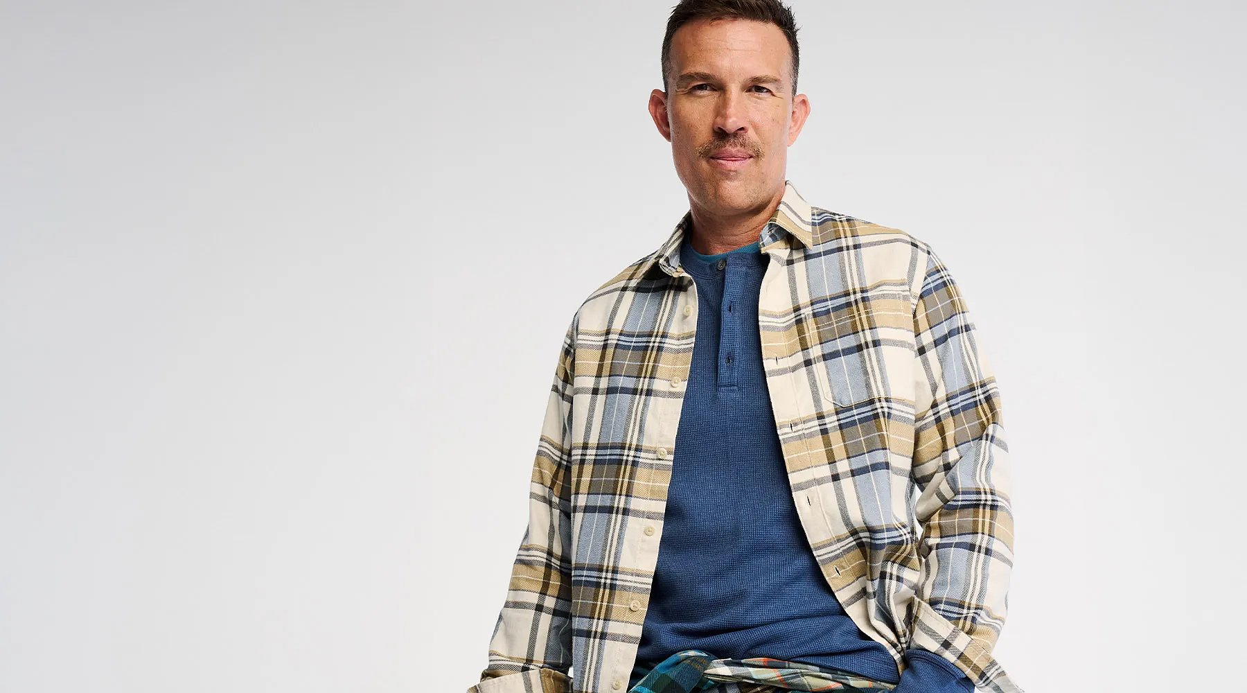 A man wears an unbuttoned flannel shirt over a T-shirt.