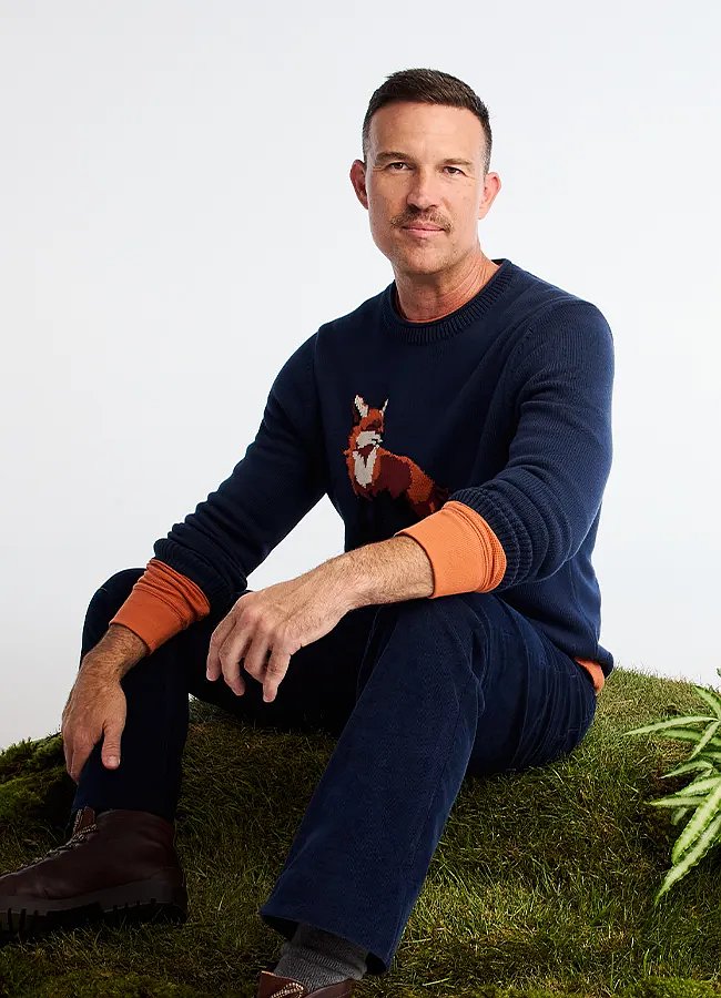 A man wearing a sweater with a fox design on the chest layered over a long-sleeve tee.