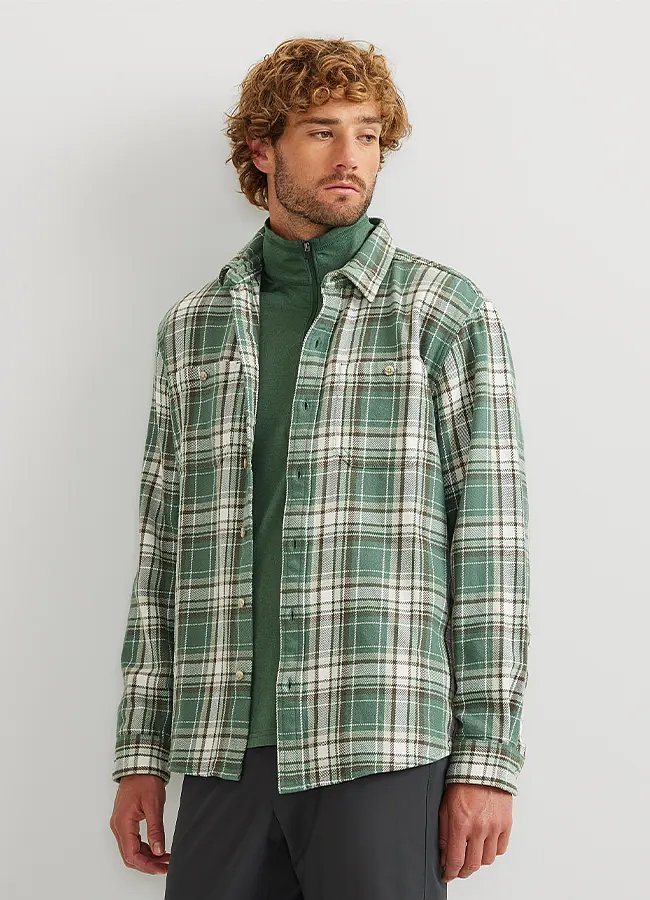 A man with curly hair and a beard wearing a flannel shirt layered over a fleece top.