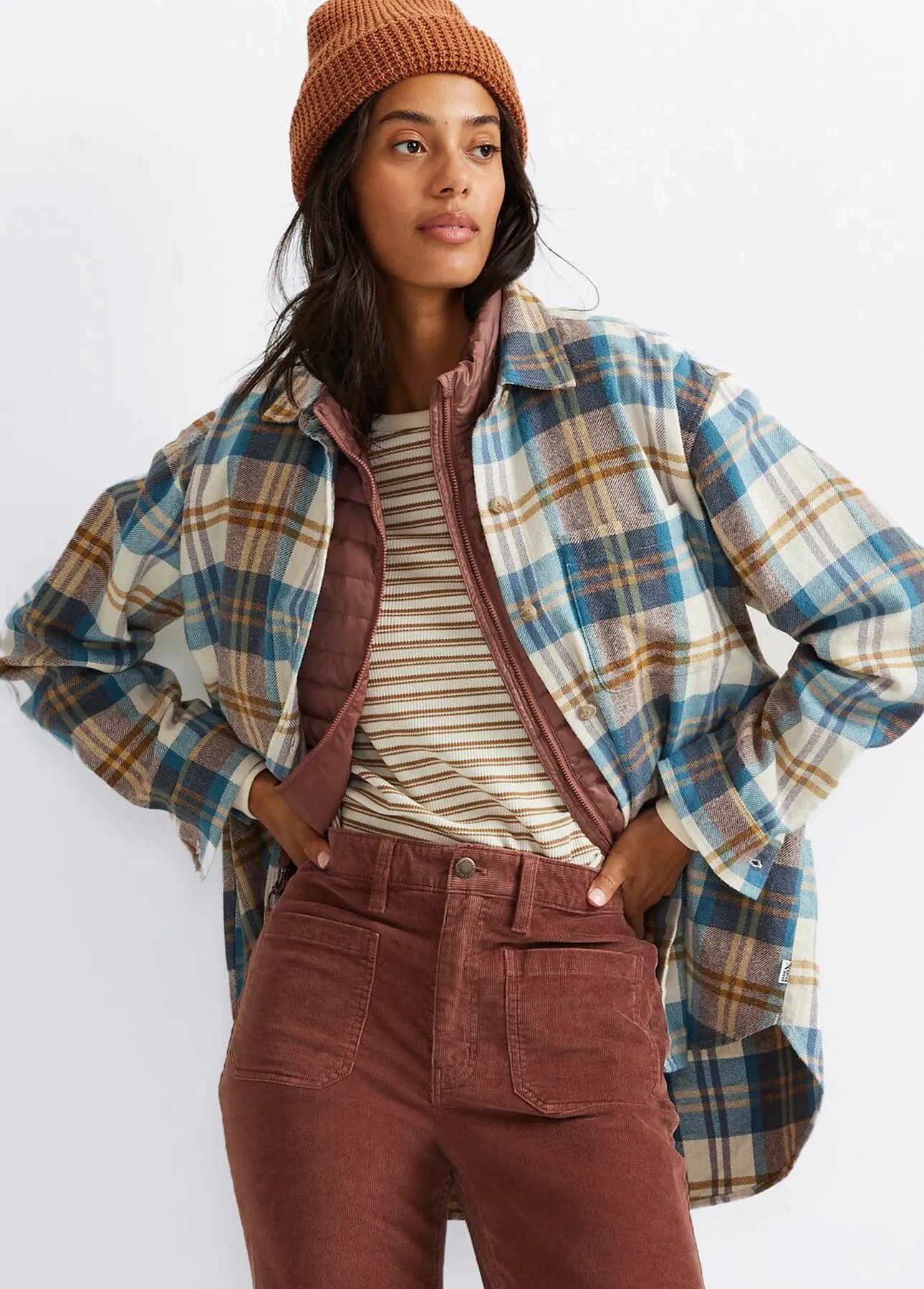 A woman wearing a flannel shirt, beanie, and corduroy pants.
