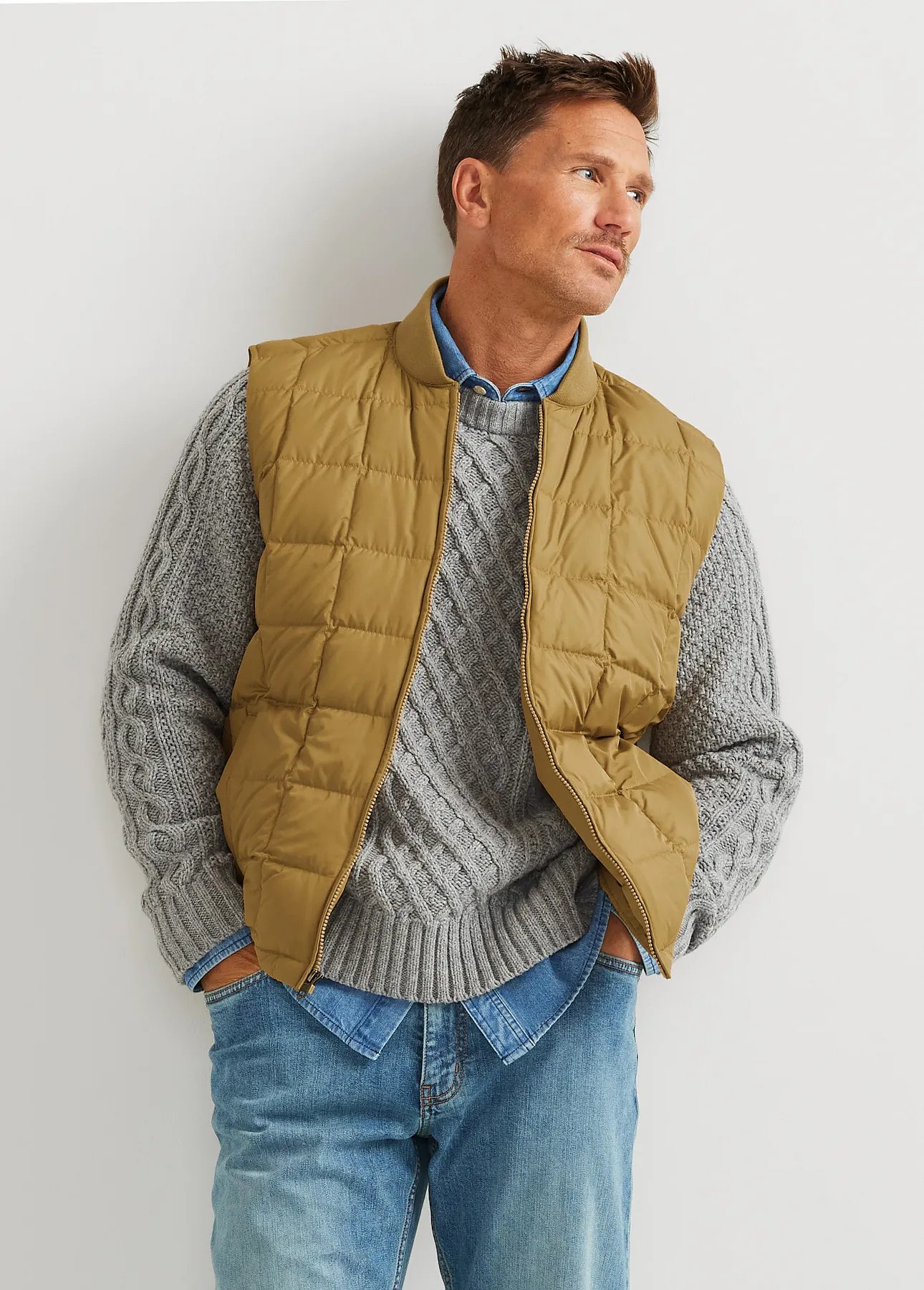 A man wears a down vest over a cable stitch sweater.